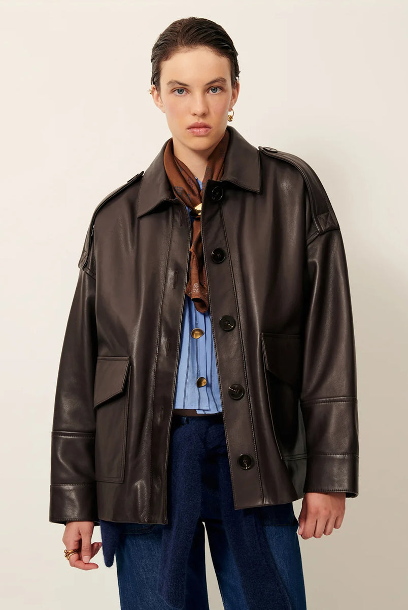 Brązowa, luźna kurtka Harriboyd Coffee Leather francuskiej marki Sessun w stylu klasycznej pilotki. Wykonana jest z gładkiej, ciemnobrązowej skóry o lekkim połysku. Z przodu zapinana jest na duże, czarne guziki, a po bogach ma duże naszywane kieszenie. Rękawy są długie, z mankietami zapinanymi na guzik. Tył kurtki jest prosty, z poziomym szwem przez plecy i elastycznym ściągaczem w dolnej części. 