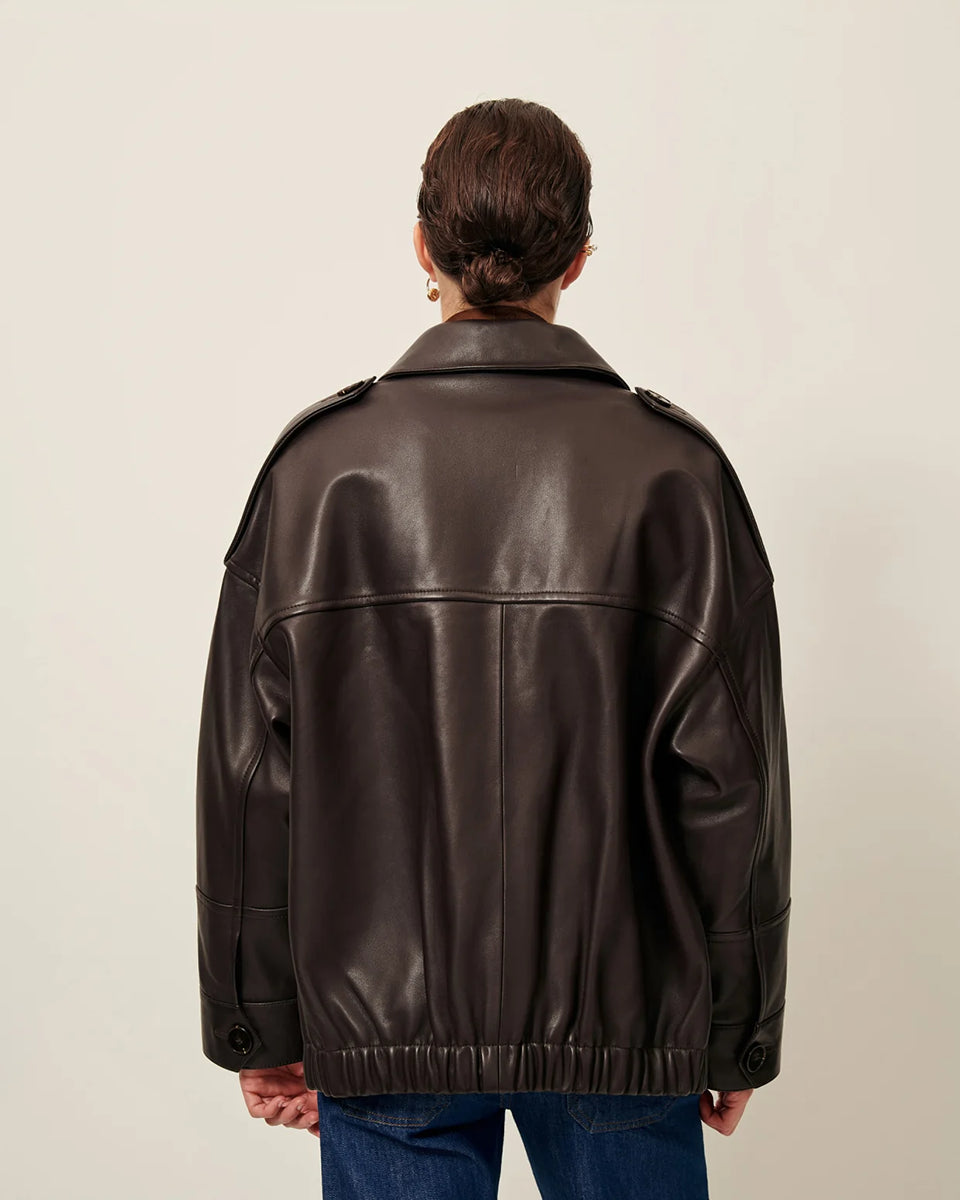 Brązowa, luźna kurtka Harriboyd Coffee Leather francuskiej marki Sessun w stylu klasycznej pilotki. Wykonana jest z gładkiej, ciemnobrązowej skóry o lekkim połysku. Z przodu zapinana jest na duże, czarne guziki, a po bogach ma duże naszywane kieszenie. Rękawy są długie, z mankietami zapinanymi na guzik. Tył kurtki jest prosty, z poziomym szwem przez plecy i elastycznym ściągaczem w dolnej części. 