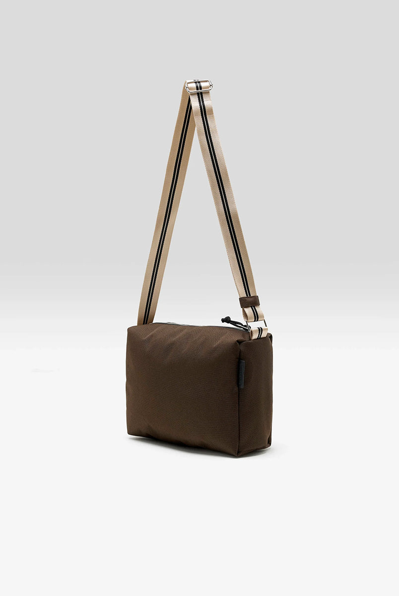 Zapinana na suwak torebka typu cross body Hobbes Dark Roast marki Bellerose z brązowego, matowego nylonu o fakturowanej powierzchni. Wyróżnia się prostokątnym kształtem, miękką konstrukcją oraz regulowanym paskiem w paski i silikonowym logo. 