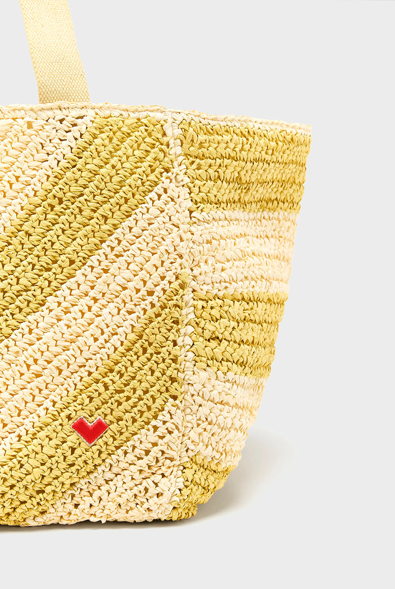 Duża, pleciona torba Ibias Stripe A marki Bellerose w faliste, kremowo-żółte paski. Posiada płócienne uchwyty i podszewkę z żółtej, bawełnianej tkaniny. W środku ma dużą kieszeń główną oraz mniejszą z logo marki. Dodatkowym detalem jest haftowane, czerwone serduszko u dołu. Wykonana z rafii. 