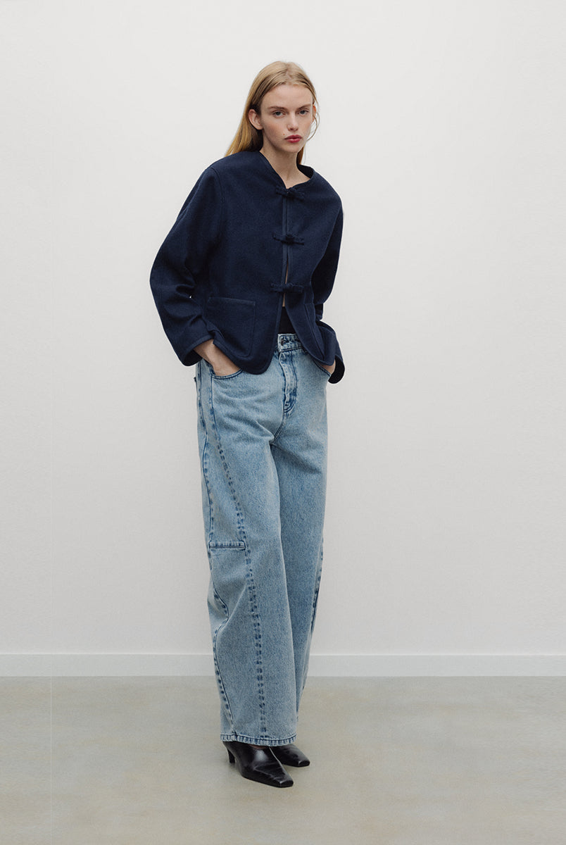 Elegancka, ciemnogranatowa, krótka kurtka Indie Black Iris o fasonie inspirowanym stylem wschodnim. Model ma prosty krój z okrągłym dekoltem bez kołnierzyka oraz długie rękawy o swobodnej linii. Charakterystycznym elementem są ozdobne, tekstylne zapięcia typu chińskiego, zwane węzełkami, które biegną wzdłuż przedniej plisy. Kurtka posiada również dwie duże, naszywane kieszenie oraz zaokrąglone doły po bokach, co nadaje jej miękki, nowoczesny wygląd. Wykonana z mieszanki z wełną.
-Inspirowana stylem wschodn