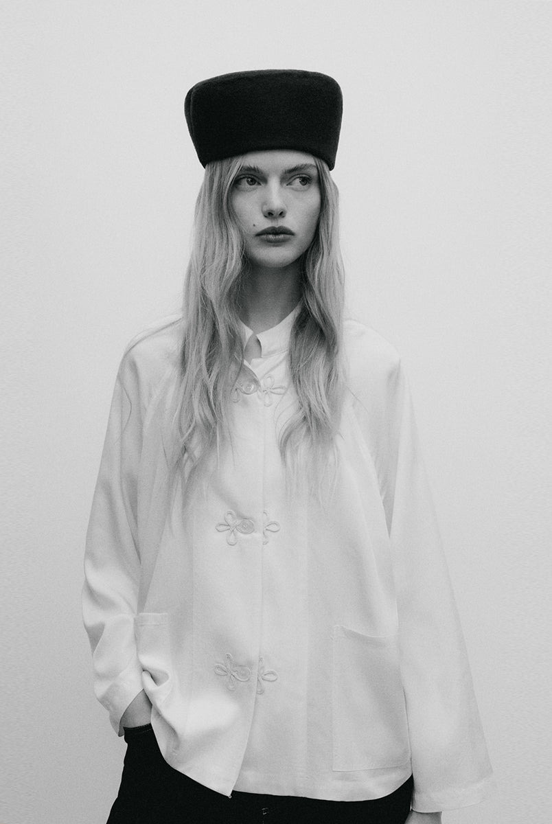 Elegancki, minimalistyczny kapelusz typu pillbox Indie TNS Black Iris wykonany z gładkiego, ciemnogranatowego filcu wełnianego. Jego konstrukcja wyróżnia się opływowym, zaokrąglonym kształtem, co nadaje mu nowoczesnego, a jednocześnie nawiązującego do stylu retro wyglądu. Kapelusz ściśle przylega do głowy, tworząc czystą, geometryczną linię, która subtelnie eksponuje rysy twarzy. 