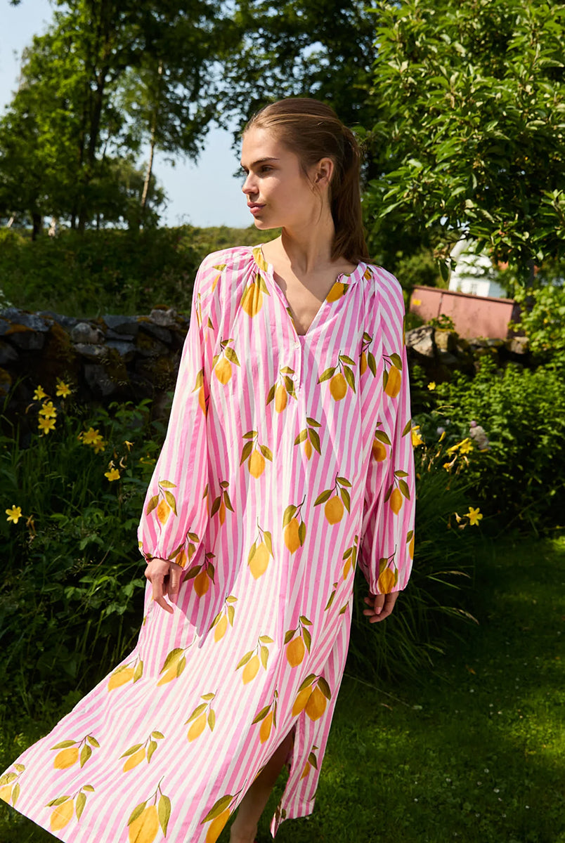 Luźna, szeroka sukienka Lara Pink Lemons SISSEL EDELBO z długimi, bufiastymi rękawami i dekoltem w serek z rozcięciem zapinanym na plisę i guziki z masy perłowej. Posiada również rozcięcia w bocznych szwach i marszczenia pod dekoltem. Ozdobiona jest pięknym, ręcznie wykonanym sitodrukiem. Wykonana w 100% z bawełny organicznej.
-Luźny krój oversize
-Ręcznie wykonany sitodruk
-100% bawełna organiczna