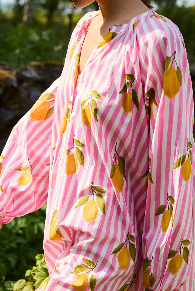 Luźna, szeroka sukienka Lara Pink Lemons SISSEL EDELBO z długimi, bufiastymi rękawami i dekoltem w serek z rozcięciem zapinanym na plisę i guziki z masy perłowej. Posiada również rozcięcia w bocznych szwach i marszczenia pod dekoltem. Ozdobiona jest pięknym, ręcznie wykonanym sitodrukiem. Wykonana w 100% z bawełny organicznej.
-Luźny krój oversize
-Ręcznie wykonany sitodruk
-100% bawełna organiczna