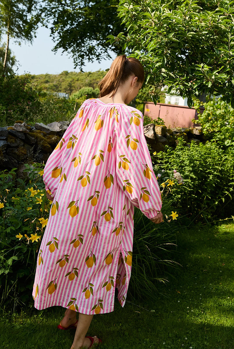 Luźna, szeroka sukienka Lara Pink Lemons SISSEL EDELBO z długimi, bufiastymi rękawami i dekoltem w serek z rozcięciem zapinanym na plisę i guziki z masy perłowej. Posiada również rozcięcia w bocznych szwach i marszczenia pod dekoltem. Ozdobiona jest pięknym, ręcznie wykonanym sitodrukiem. Wykonana w 100% z bawełny organicznej.
-Luźny krój oversize
-Ręcznie wykonany sitodruk
-100% bawełna organiczna