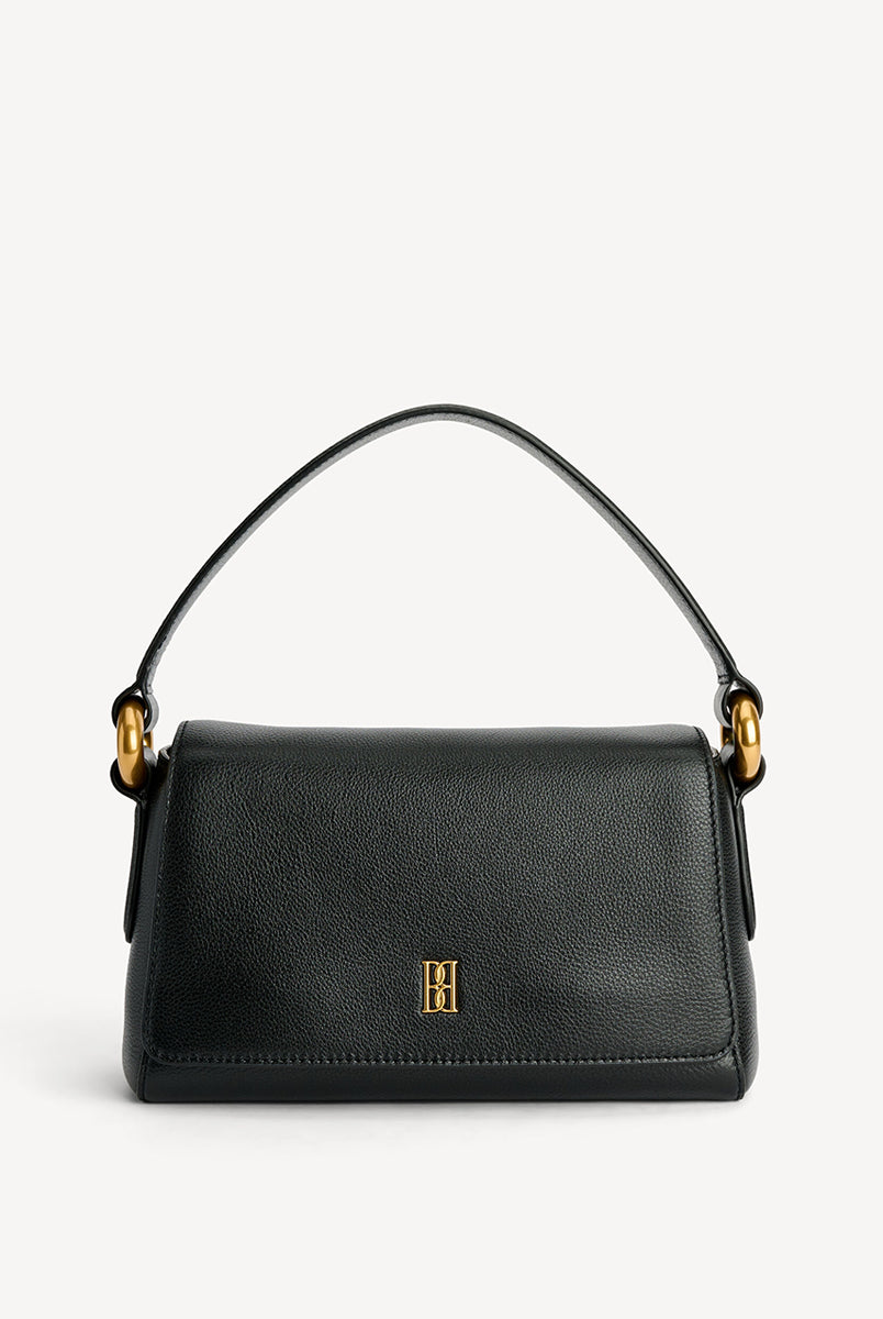 Minimalistyczna, elegancka torebka Lellie Black By Malene Birger o prostokątnym kształcie z lekko zaokrąglonymi bokami. Zapinana na zatrzask magnetyczny. Posiada krótki, szeroki pasek na ramię, który ozdobiony jest złotymi elementami. Na środku klapy umieszczono metalowy emblemat marki w kolorze złotym. W środku znajduje się mała kieszonka na drobiazgi, a całość wykończona jest gładką podszewką. Wykonana w 100% ze skóry. 
