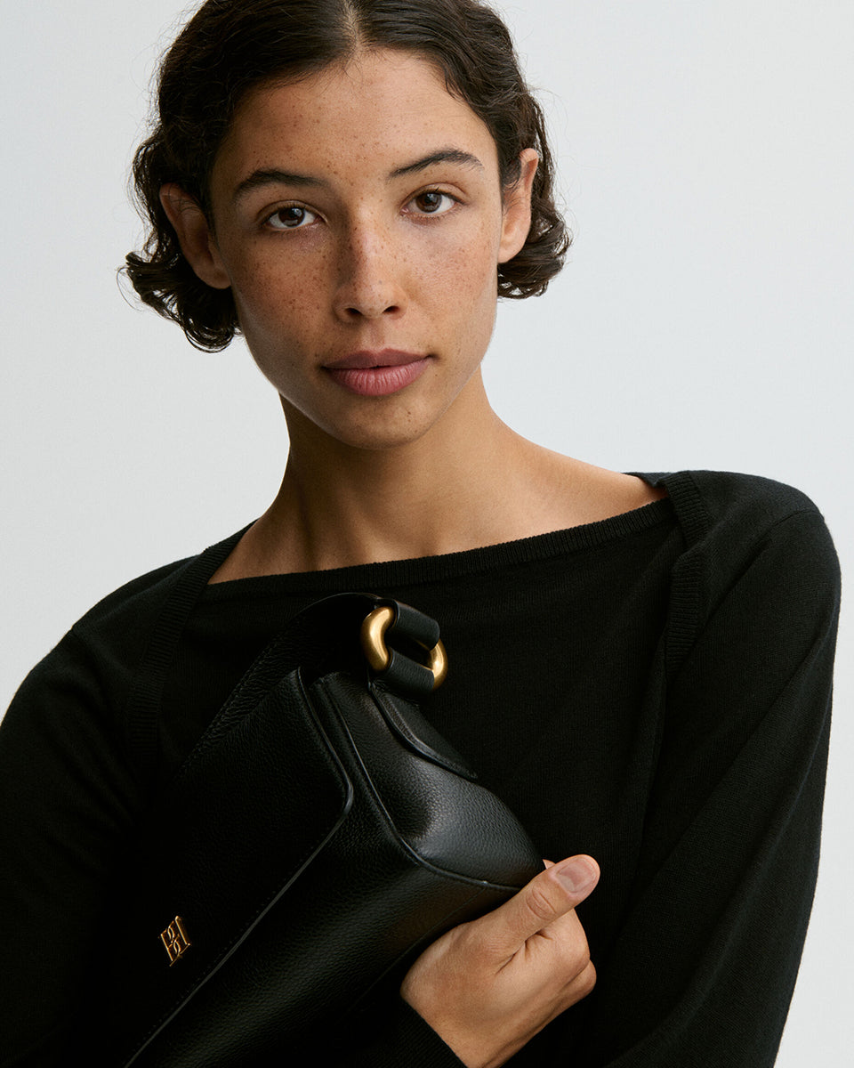 Minimalistyczna, elegancka torebka Lellie Black By Malene Birger o prostokątnym kształcie z lekko zaokrąglonymi bokami. Zapinana na zatrzask magnetyczny. Posiada krótki, szeroki pasek na ramię, który ozdobiony jest złotymi elementami. Na środku klapy umieszczono metalowy emblemat marki w kolorze złotym. W środku znajduje się mała kieszonka na drobiazgi, a całość wykończona jest gładką podszewką. Wykonana w 100% ze skóry. 