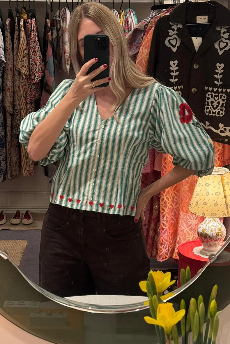 Kobieca bluzka koszulowa Lotta Green Stripes SISSEL EDELBO z dopasowaną talią i marszczeniem z tyłu. Ma głęboki dekolt w serek i zapięcie z przodu na guziki z masy perłowej. Rękawy mają długość 3/4 i zakończone są gumką. Ozdobiona jest delikatnym haftem kwiatowym i serduszkami. Wykonana z organicznej bawełny popelinowej w paski.
-Dopasowana talia
-100% bawełna organiczna
-Zamów bluzkę w swoim standardowym rozmiarze 