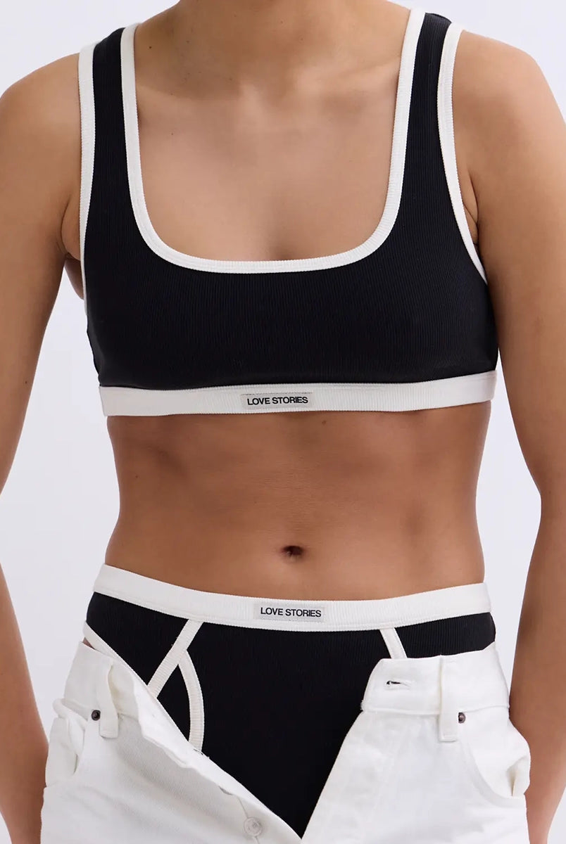 Miękki sportowy stanik top Rika Love Love Stories na grubych ramiączkach. Wykonany z miękkiej tkaniny z prążkowaną fakturą i białą, grubą lamówką. Na gumie pod biustem posiada niewielką naszywkę z logo marki. 
