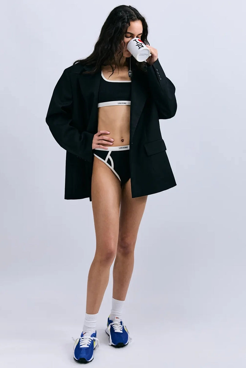 Miękki sportowy stanik top Rika Love Love Stories na grubych ramiączkach. Wykonany z miękkiej tkaniny z prążkowaną fakturą i białą, grubą lamówką. Na gumie pod biustem posiada niewielką naszywkę z logo marki. 