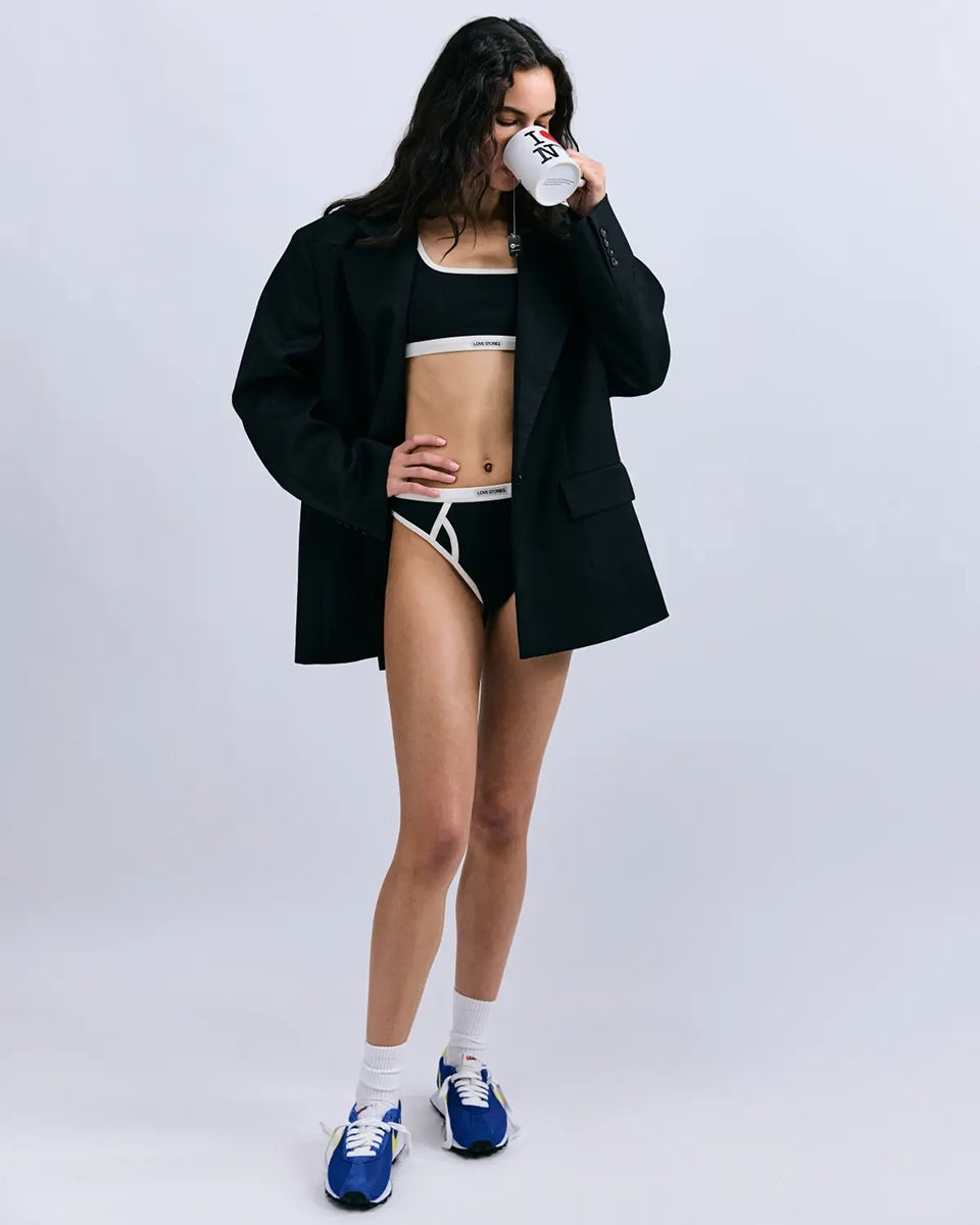 Miękki sportowy stanik top Rika Love Love Stories na grubych ramiączkach. Wykonany z miękkiej tkaniny z prążkowaną fakturą i białą, grubą lamówką. Na gumie pod biustem posiada niewielką naszywkę z logo marki. 