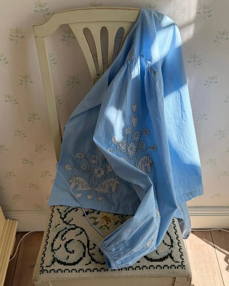 Luźna, krótka bluzka Maggan Light Blue SISSEL EDELBO z szerokimi, obszernymi rękawami z marszczeniami na ramionach. Rękawy zakończone są gumką. Dekolt jest delikatnie wyprofilowany i wiązany z przodu na dwa sznurki. Bluzkę zdobi haft z delikatnymi koralikami. 