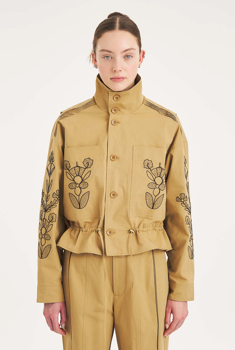 Krótka, strukturalna kurtka Maria Beige Antik Batik o nowoczesnym, nieco geometrycznym kroju. Posiada charakterystyczną, bardzo wysoką stójkę zapinaną na guziki. Regulowana w pasie za pomocą ściągacza ze sznurkami, co tworzy efekt delikatnej baskinki/falbany. Z przodu na kieszeniach oraz na rękawach znajdują się hafty z motywami roślinnymi i kwiatowymi. Dodatkowe, drobne, haftowane przeszycia ozdabiają również linię ramion. Zapinana na guziki.
-Krótki, nowoczesny fason
-Hafty z motywami roślinnymi i