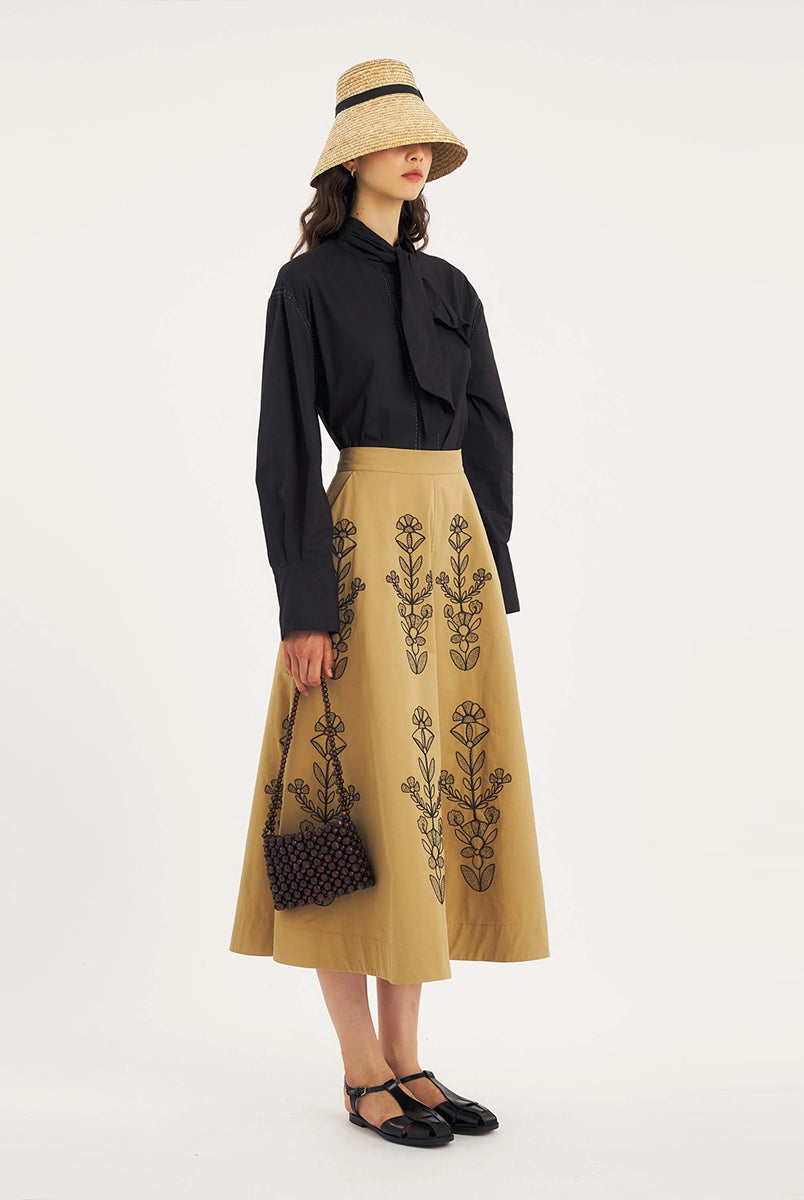 Rozkloszowana, trapezowa spódnica Maria Beige marki Antik Batik o klasycznej długości midi, sięgającej do połowy łydki. Ma wysoką, gładką talię z wyraźnie zaznaczonym, szerokim pasem. Głównym elementem dekoracyjnym są duże, pionowe hafty roślinne i kwiatowe w ciemnym kolorze. Haft układa się symetrycznie, w pionowe rzędy, co optycznie wydłuża sylwetkę i nadaje całości tradycyjny, rzemieślniczy charakter.
-Długość midi
-Wysoki stan
-Ozdobne hafty kwiatowe i roślinne
-Zamów spódnicę w swoim standard