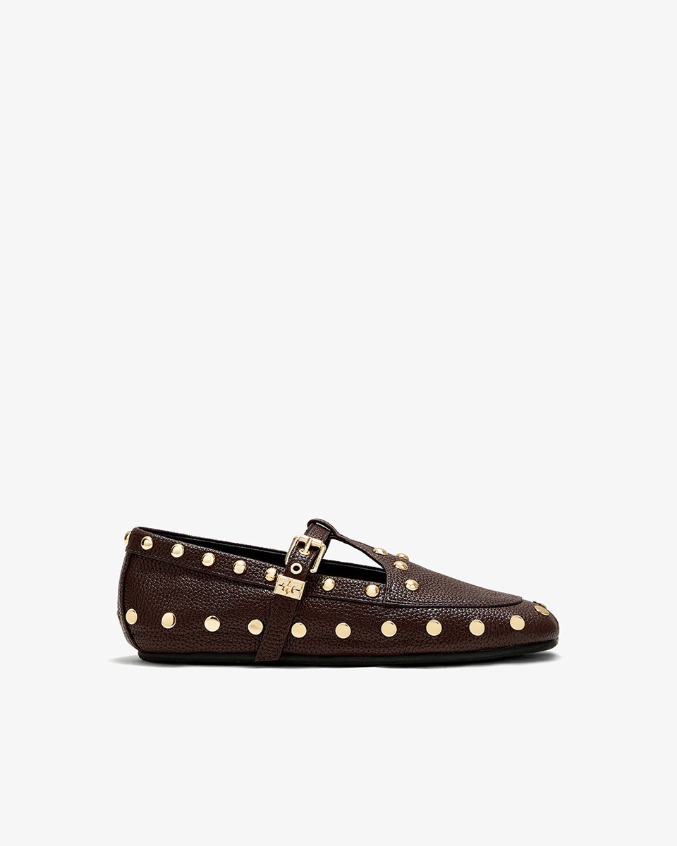 Płaskie, ciemnobrązowe mokasyny Mary Jenny Studs GANNI Chicory Coffee o zaokrąglonych noskach. Cholewkę zdobią liczne, gęsto rozmieszczone złote piny (ćwieki). Posiadają regulowane paski zapinane na złotą klamrę zakończoną charakterystycznym logo GANNI Butterfly po zewnętrznej stronie stopy. Buty mają wyraźną, groszkowaną fakturę. Rozmiarówka jest standardowa, a wysokość obcasa to 0,7 cm.
-Standardowa rozmiarówka