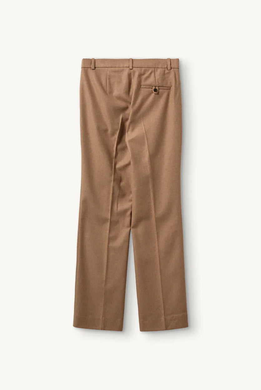 Proste, eleganckie spodnie Mitch Camel o klasycznym, lekko luźnym kroju z długimi nogawkami. Mają średni stan z dopasowanym pasem i zaszewkami z przodu, co podkreśla sylwetkę i dodaje formalnego charakteru. Z tyłu znajdują się kieszenie z lamówkami, a jedna z nich zapinana jest na guzik. Wykonane z tkaniny z wełną z recyklingu.