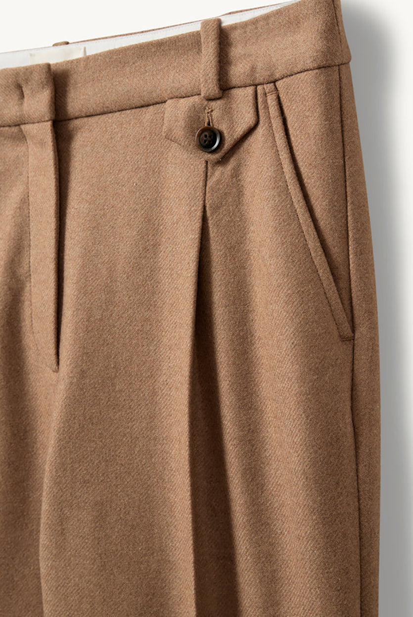 Proste, eleganckie spodnie Mitch Camel o klasycznym, lekko luźnym kroju z długimi nogawkami. Mają średni stan z dopasowanym pasem i zaszewkami z przodu, co podkreśla sylwetkę i dodaje formalnego charakteru. Z tyłu znajdują się kieszenie z lamówkami, a jedna z nich zapinana jest na guzik. Wykonane z tkaniny z wełną z recyklingu.