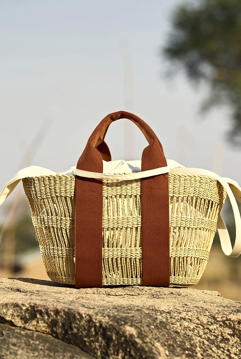 Średniej wielkości, ręcznie pleciony, częściowo ażurowy kosz GEORGE NET - NATURAL x RUST HDL x ECRU COTTON francuskiej marki Muun. Posiada trapezowy kształt, dwie mocne, materiałowe rączki do wygodnego trzymania w dłoni oraz długi, cienki pasek do zawieszenia na ramieniu.