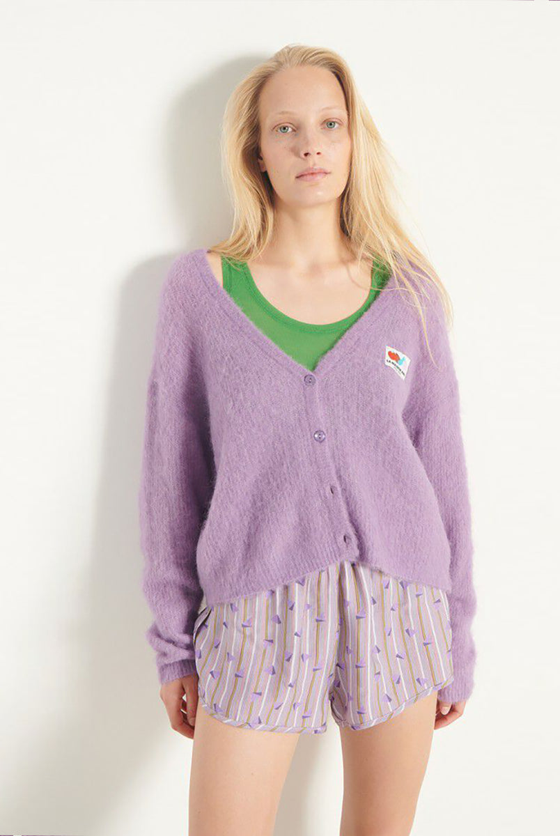 Oversizowy, miękki kardigan Nenybay Violet marki American Vintage z długim rękawem i dekoltem w serek. Zapinany na guziki. Posiada naszywkę z logo na piersi. Zakończony ściągaczami. Wykonany z lekkiej dzianiny z alpaką. Noś go samodzielnie lub połącz z innymi elementami garderoby, aby stworzyć warstwowy, codzienny look. 