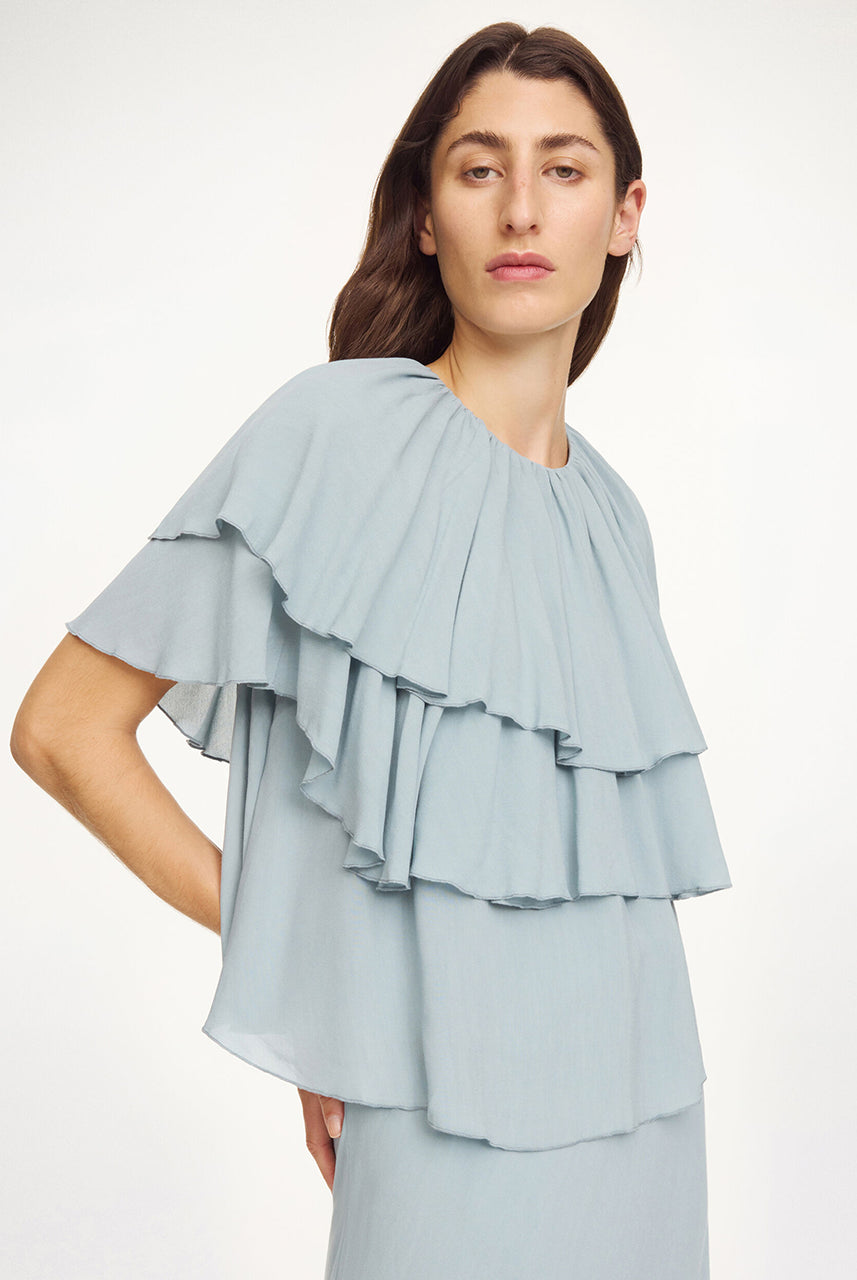 Luźny, błękitny top Nina Arona Blue By Malene Birger z okrągłym dekoltem i wiązaniem z tyłu. Składa się z kilku, półprzezroczystych warstw. Pierwsza falbana opada na ramiona, tworząc efekt 'rękawa skrzydełka'. Wykonany z wiskozy.
-Luźny, swobodny fason
-Bez rękawów
-Zamów w swoim standardowym rozmiarze 