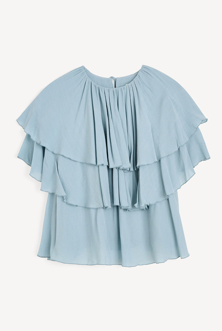 Luźny, błękitny top Nina Arona Blue By Malene Birger z okrągłym dekoltem i wiązaniem z tyłu. Składa się z kilku, półprzezroczystych warstw. Pierwsza falbana opada na ramiona, tworząc efekt 'rękawa skrzydełka'. Wykonany z wiskozy.
-Luźny, swobodny fason
-Bez rękawów
-Zamów w swoim standardowym rozmiarze 