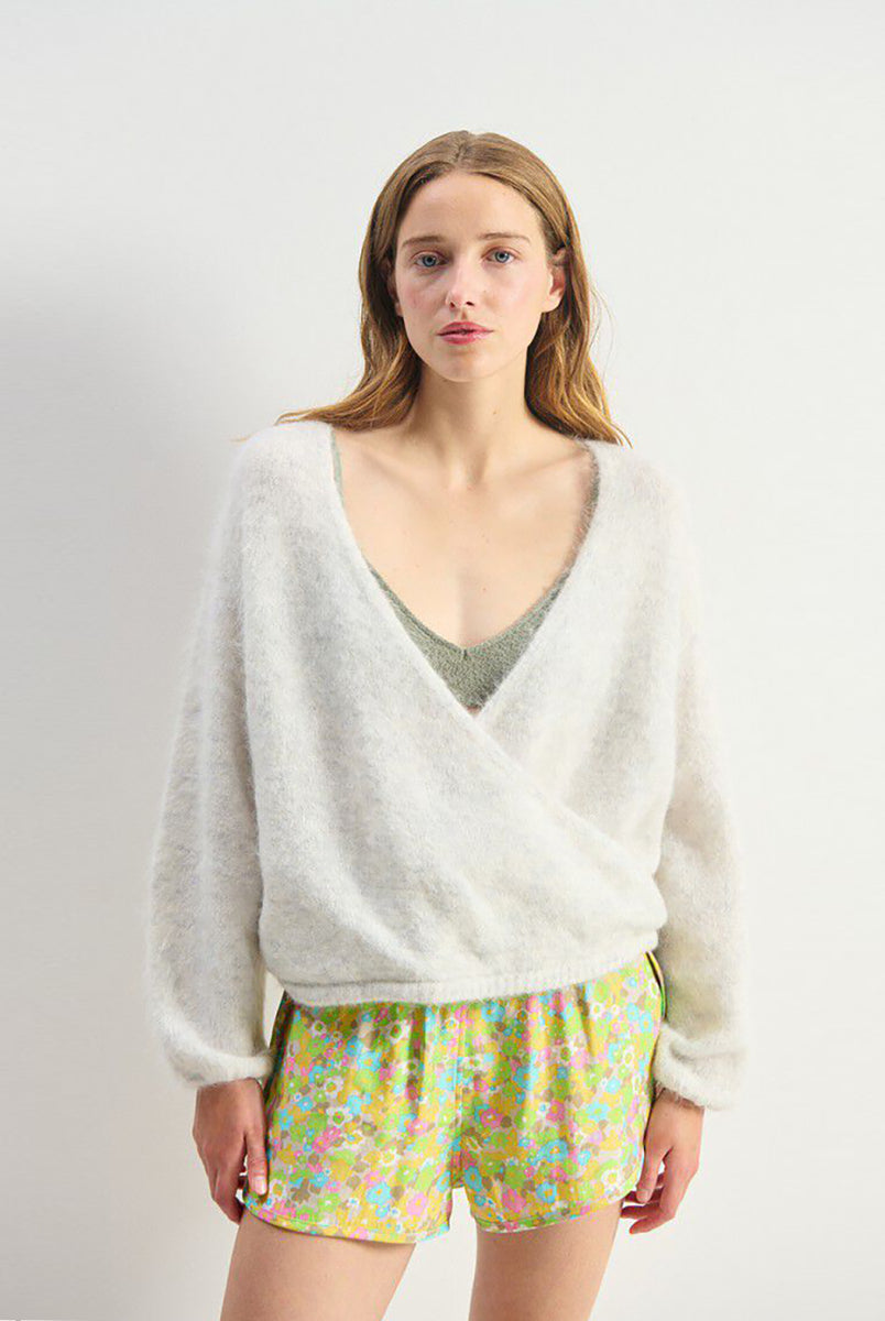 Miękki, krótki sweter NUN18 Polar Melange marki American Vintage z długimi rękawami i głębokim, skrzyżowanym kołnierzem. Wykończony ściągaczami. Wykonany z ciepłej dzianiny z alpaką. Jego kulisty kształt i kopertowy dekolt sprawiają, że jest to kobiecy, a zarazem wygodny element garderoby. Noś go z jeansami, spódnicą lub legginsami. 