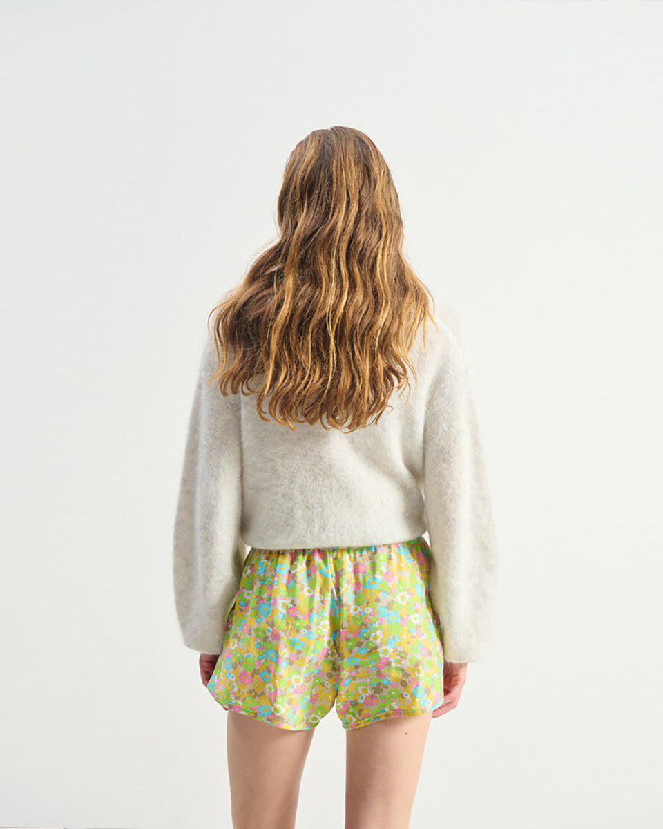 Miękki, krótki sweter NUN18 Polar Melange marki American Vintage z długimi rękawami i głębokim, skrzyżowanym kołnierzem. Wykończony ściągaczami. Wykonany z ciepłej dzianiny z alpaką. Jego kulisty kształt i kopertowy dekolt sprawiają, że jest to kobiecy, a zarazem wygodny element garderoby. Noś go z jeansami, spódnicą lub legginsami. 