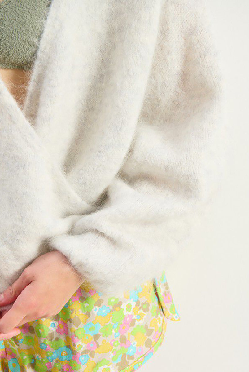 Miękki, krótki sweter NUN18 Polar Melange marki American Vintage z długimi rękawami i głębokim, skrzyżowanym kołnierzem. Wykończony ściągaczami. Wykonany z ciepłej dzianiny z alpaką. Jego kulisty kształt i kopertowy dekolt sprawiają, że jest to kobiecy, a zarazem wygodny element garderoby. Noś go z jeansami, spódnicą lub legginsami. 