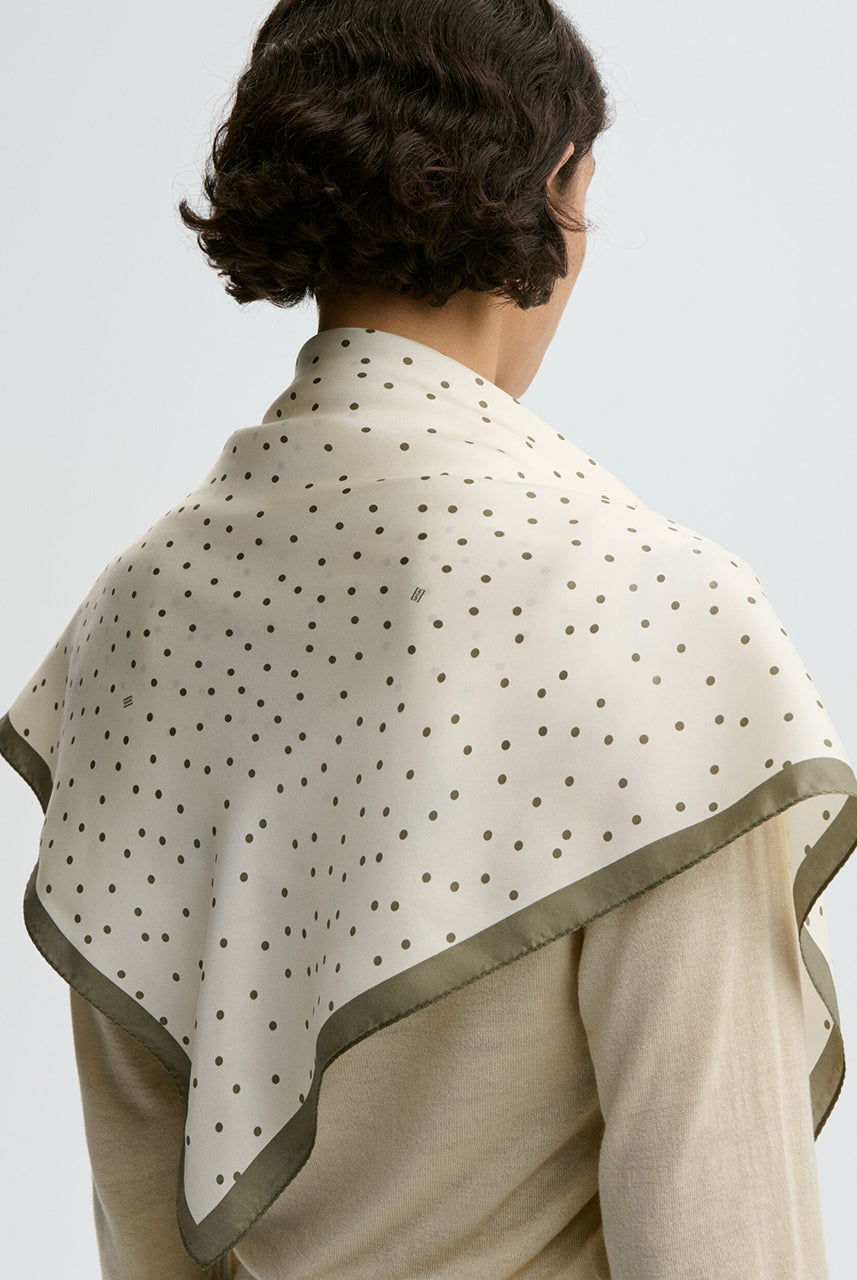 Klasyczna, piękna chusta Poulas Deep Lichen Green By Malene Birger w ponadczasowy wzór polka dots i kontrastową krawędzią. Wykonana z luksusowego jedwabiu. Zawiąż ją na szyi, nadgarstku lub rączce torebki.