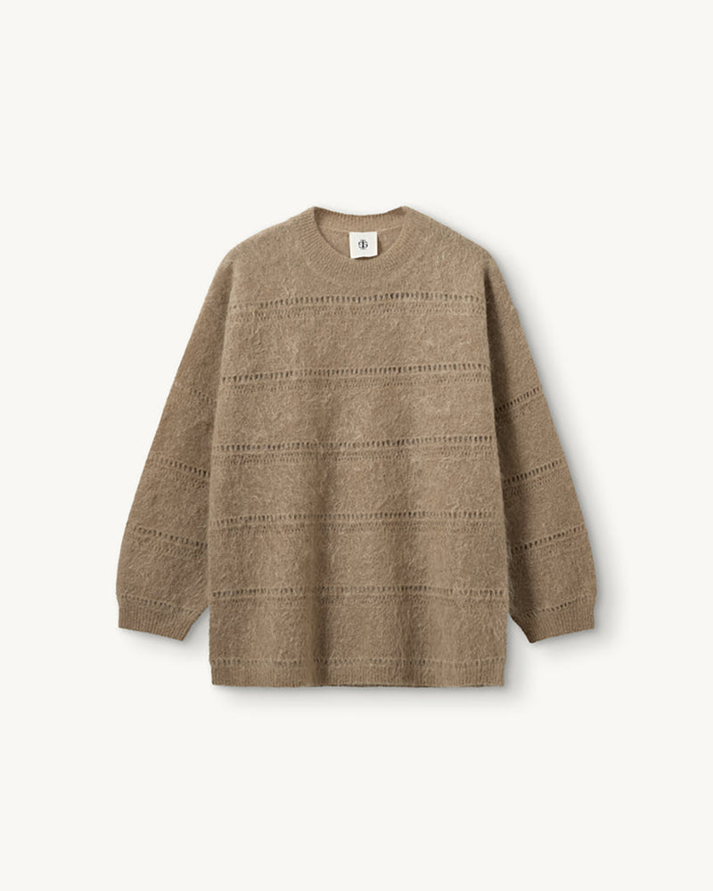Luźny, oversizowy sweter Roma The Garment w klasycznym odcieniu jasnego brązu. Posiada prosty, okrągły dekolt i lekko opadające ramiona. Sweter ma długie rękawy. Jego powierzchnię wyróżnia urozmaicona faktura- gładką dzianinę przeplatają poziome pasy o dekoracyjnym, ażurowym splocie, które dodają całości lekkości i unikalnego charakteru. Jest wykończony ściągaczami. Wykonany z puchatej dzianiny z moherem.
-Luźny fason
-Okrągły dekolt
-Dzianina z moherem
-Zamów sweter w swoim normalnym rozmiarze