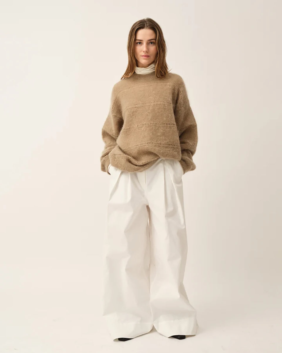 Luźny, oversizowy sweter Roma The Garment w klasycznym odcieniu jasnego brązu. Posiada prosty, okrągły dekolt i lekko opadające ramiona. Sweter ma długie rękawy. Jego powierzchnię wyróżnia urozmaicona faktura- gładką dzianinę przeplatają poziome pasy o dekoracyjnym, ażurowym splocie, które dodają całości lekkości i unikalnego charakteru. Jest wykończony ściągaczami. Wykonany z puchatej dzianiny z moherem.
-Luźny fason
-Okrągły dekolt
-Dzianina z moherem
-Zamów sweter w swoim normalnym rozmiarze