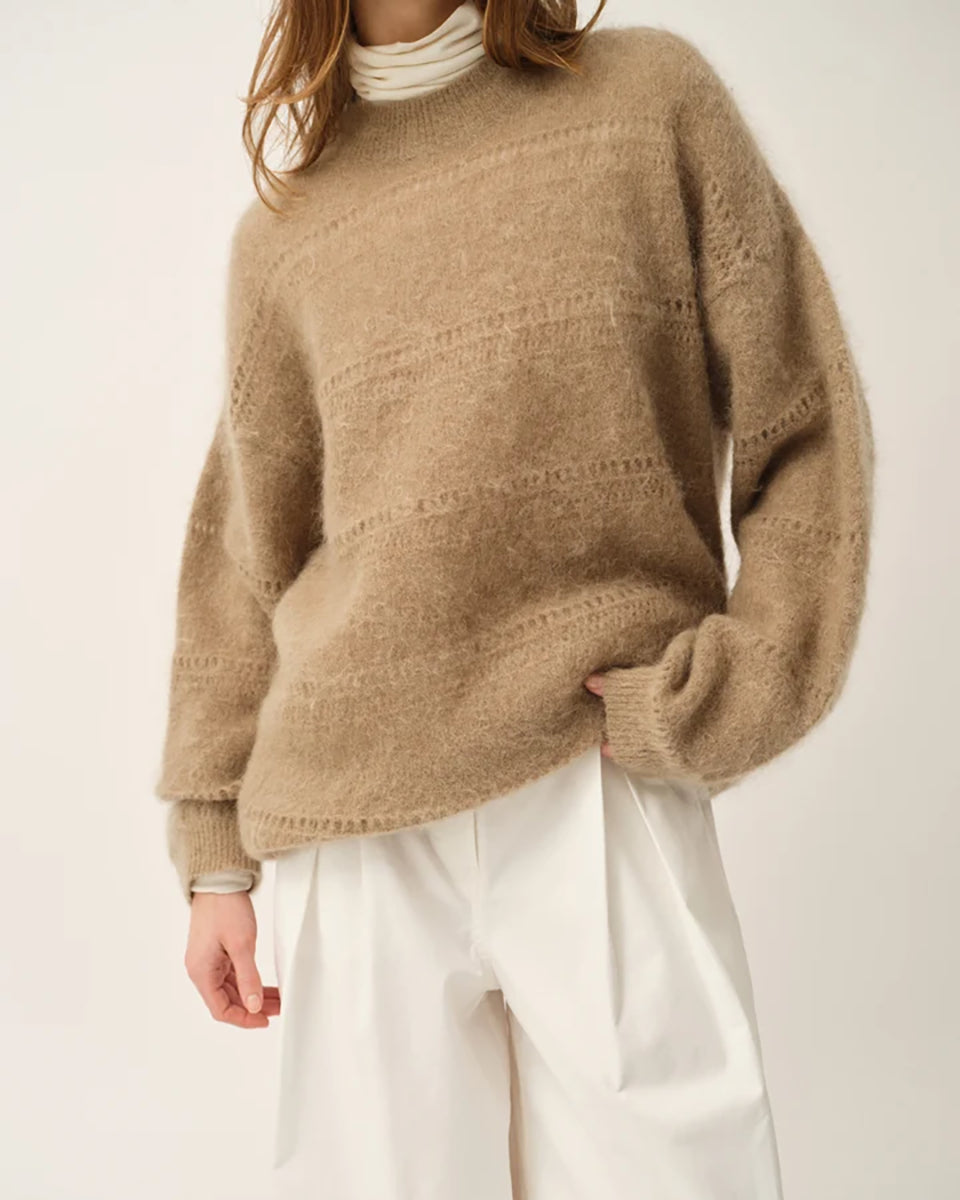 Luźny, oversizowy sweter Roma The Garment w klasycznym odcieniu jasnego brązu. Posiada prosty, okrągły dekolt i lekko opadające ramiona. Sweter ma długie rękawy. Jego powierzchnię wyróżnia urozmaicona faktura- gładką dzianinę przeplatają poziome pasy o dekoracyjnym, ażurowym splocie, które dodają całości lekkości i unikalnego charakteru. Jest wykończony ściągaczami. Wykonany z puchatej dzianiny z moherem.
-Luźny fason
-Okrągły dekolt
-Dzianina z moherem
-Zamów sweter w swoim normalnym rozmiarze