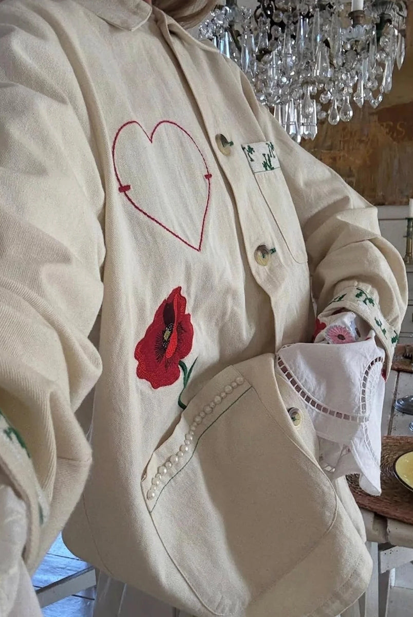 Cienka, luźna, koszulowa kurtka Bea SISSEL EDELBO z kołnierzykiem i długimi rękawami zakończonymi mankietami. Zapinana na duże guziki. Kurtka posiada trzy, duże, prostokątne kieszenie z przodu. Dolne kieszenie obszyte zostały drobnymi perełkami. Kurtka dekorowana jest efektownymi haftami z motywami kwiatów, serca i biedronki