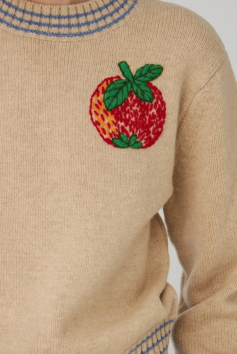 Krótki, beżowy sweter STELLA NOVA z dużym, haftowanym jabłkiem nad lewą piersią. Sweter ma okrągły dekolt i opadające ramiona. Wykończony jest ściągaczami i niebieskimi paskami przy dekolcie, mankietach i u dołu.