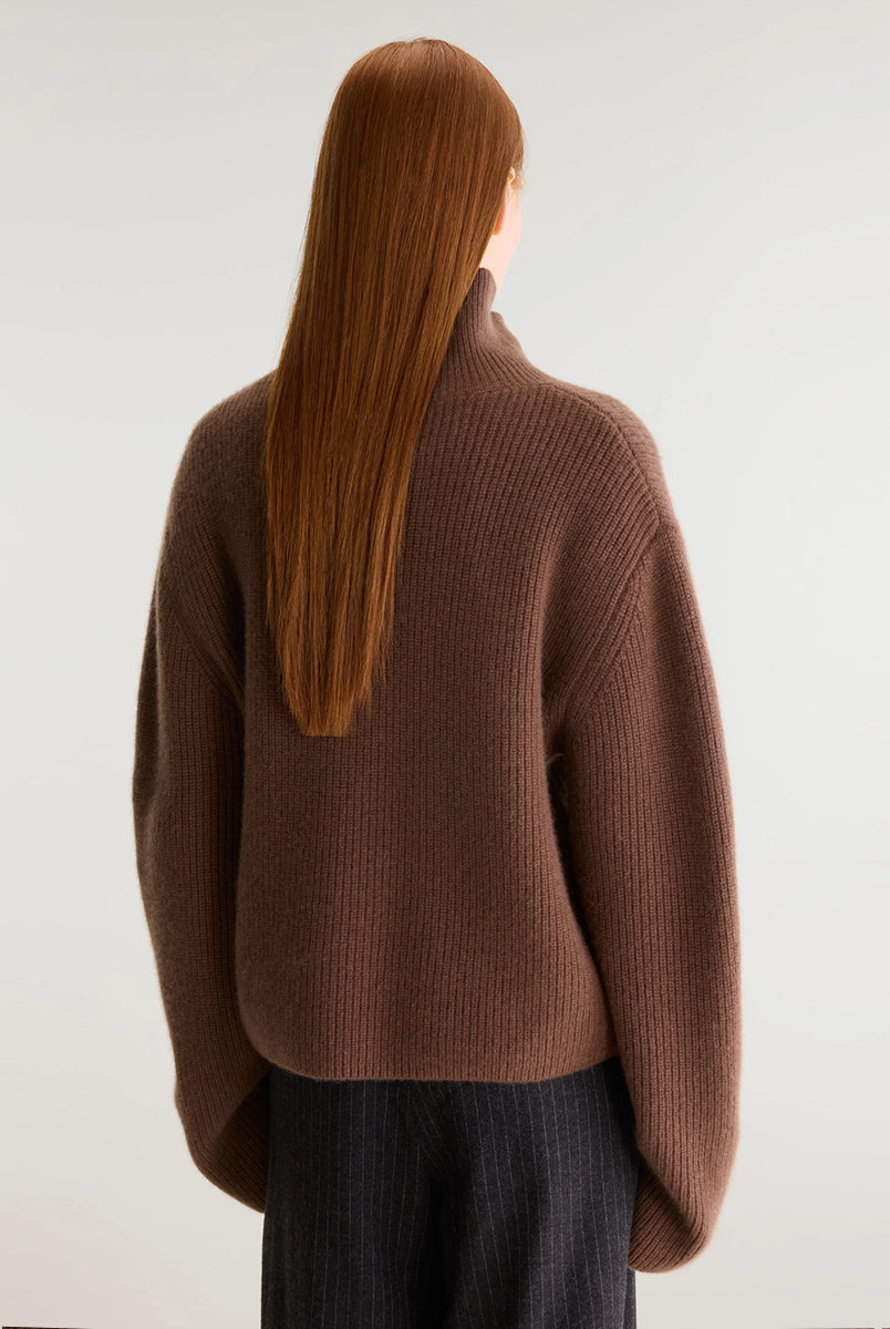 Luźny, brązowy sweter z golfem Synin Tiramisu Bellerose wykonany w 100% z kaszmiru. Posiada proste, szerokie rękawy z wywiniętymi mankietami i kołnierz typu funnel neck. Ma swobodny, lekko luźny krój oraz wyraźną, prążkowaną strukturę materiału. Wysoki, otulający golf dodaje mu szyku i doskonale sprawdza się w chłodniejsze dni, tworząc stylową kompozycję z ciemnymi spodniami.
-Golf
-Długie, szerokie rękawy
-100% kaszmir