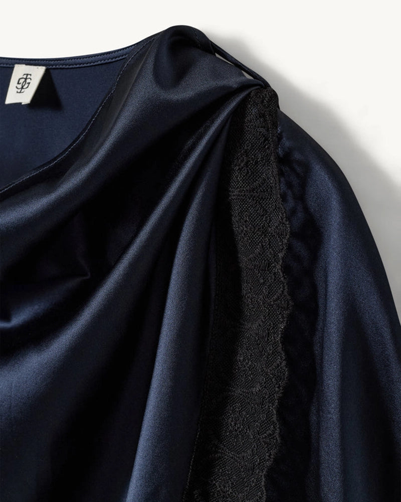 Elegancka, jedwabna peleryna Cata The Garment o asymetrycznym fasonie. Zebrana na lewym ramieniu. Wykończona zmysłową koronką. Wykonana z lejącej, jedwabnej tkaniny.