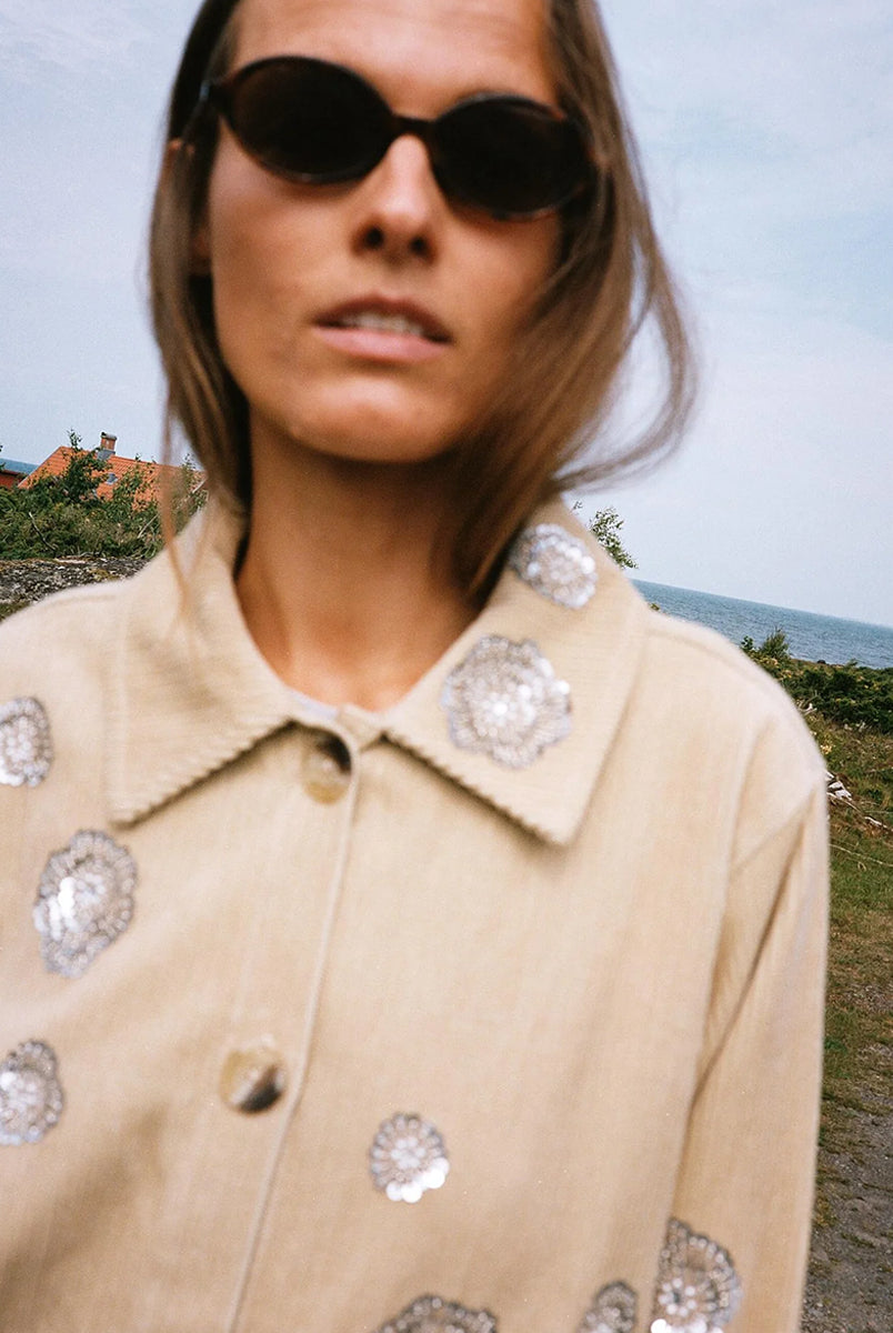 Luźna, sztruksowa kurtka Twiggy Golden Beige SISSEL EDELBO o swobodnym kroju, z małym, koszulowym kołnierzykiem i długimi rękawami. Posiada dwie kieszenie z przodu i zapięcie na guziki. Zdobiona jest cekinami i koralikowymi rozetami o różnych rozmiarach, ułożonymi w nieregularny wzór.
-Luźny fason
-100% bawełna organiczna