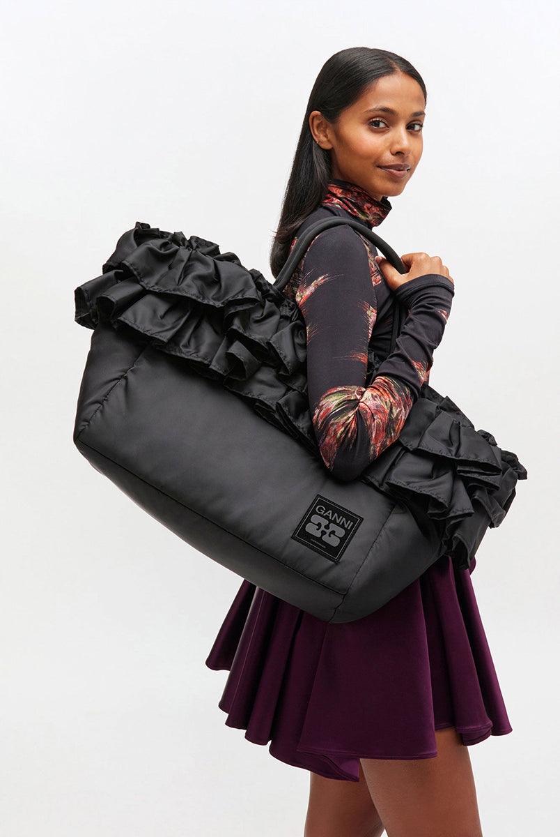 Torba typu tote 7188 XXL Shopper Black marki GANNI z uchwytami. Posiada jedną dużą komorę z wewnętrzną kieszenią zapinaną na zamek. U dołu znajduje się niewielkie logo marki. Wyjątkowości dodaje zdobienie w postaci falbanek. Zaprojektowana, aby pomieścić telefon, portfel, okulary przeciwsłoneczne, klucze, butelkę z wodą, saszetkę, strój sportowy i laptopa.