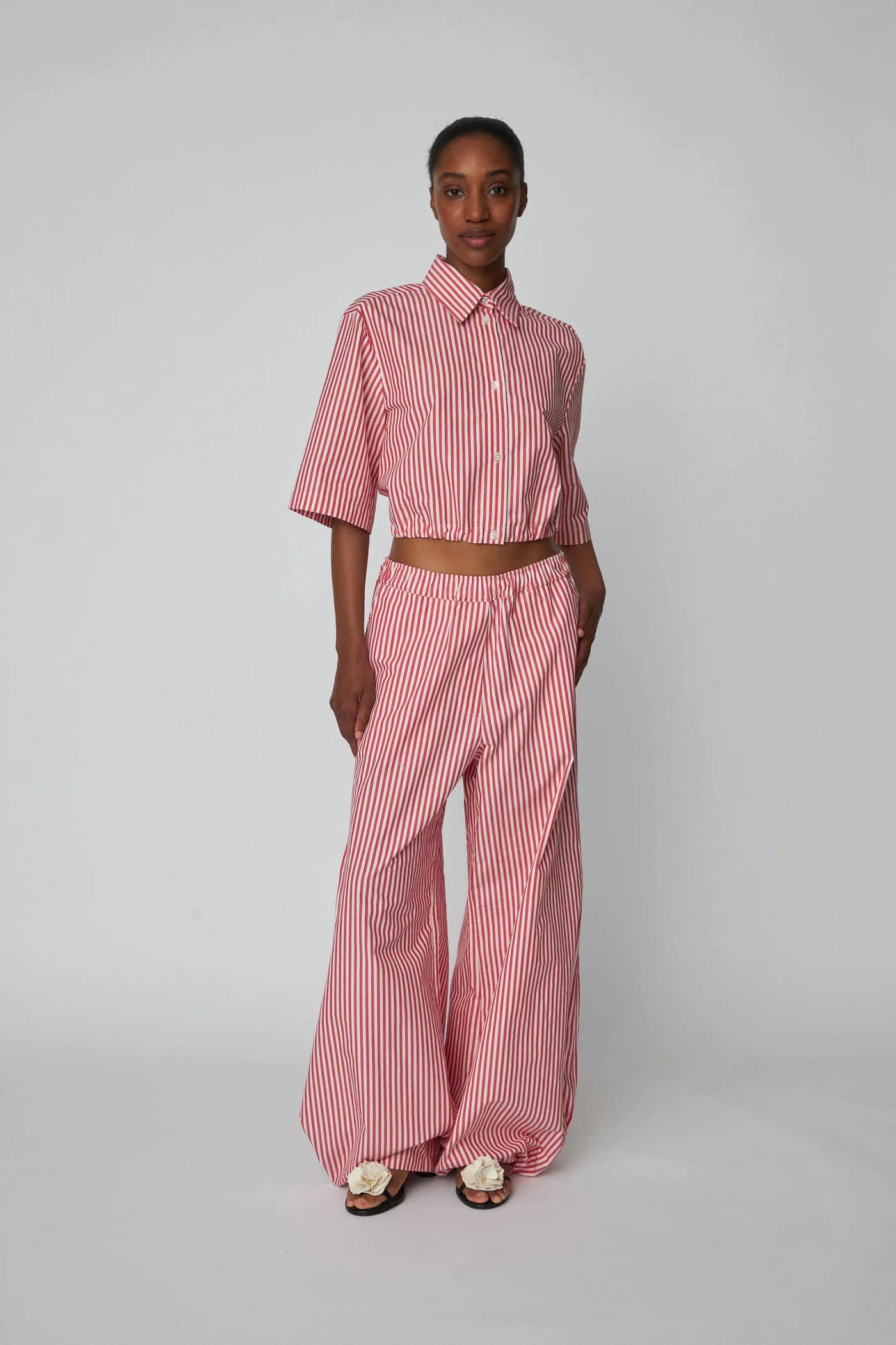 Oversizowe, bawełniane spodnie w czerwono-białe paski Oversized Striped STELLA NOVA z szerokimi i długimi nogawkami ściąganymi u dołu za pomocą gumek. Spodnie mają wysoki stan i elastyczną talię.