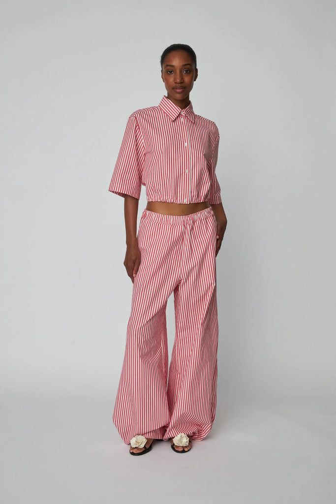 Oversizowe, bawełniane spodnie w czerwono-białe paski Oversized Striped STELLA NOVA z szerokimi i długimi nogawkami ściąganymi u dołu za pomocą gumek. Spodnie mają wysoki stan i elastyczną talię.