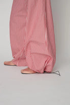 Oversizowe, bawełniane spodnie w czerwono-białe paski Oversized Striped STELLA NOVA z szerokimi i długimi nogawkami ściąganymi u dołu za pomocą gumek. Spodnie mają wysoki stan i elastyczną talię.