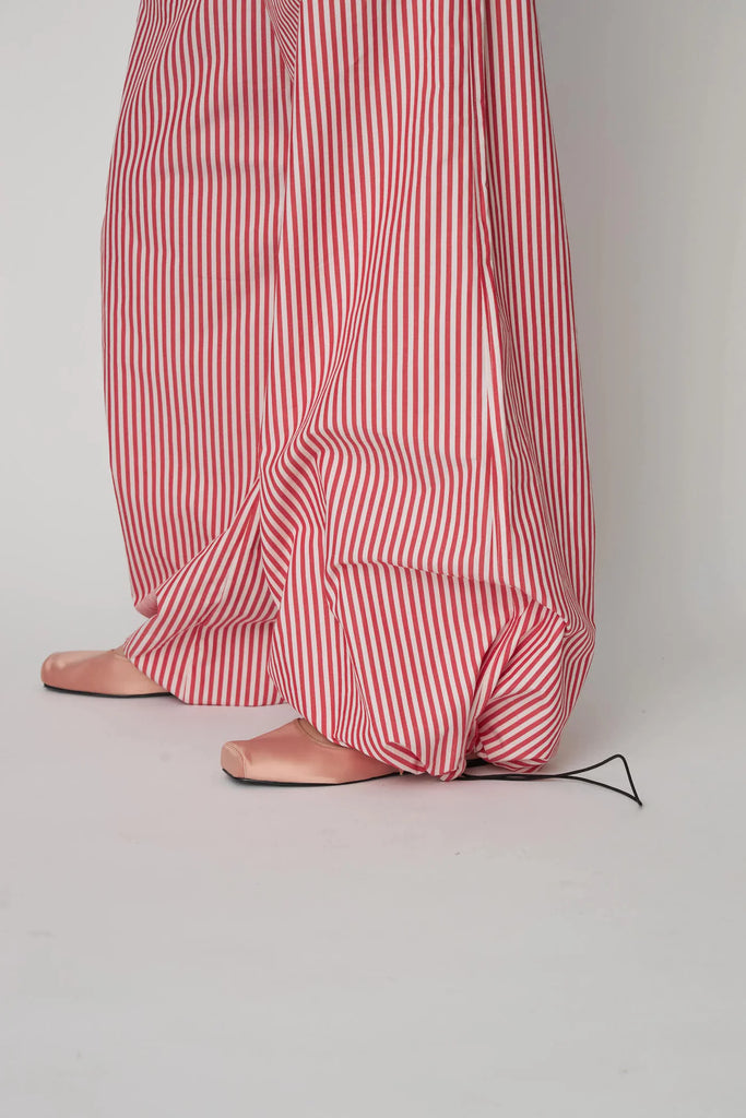 Oversizowe, bawełniane spodnie w czerwono-białe paski Oversized Striped STELLA NOVA z szerokimi i długimi nogawkami ściąganymi u dołu za pomocą gumek. Spodnie mają wysoki stan i elastyczną talię.
