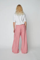 Oversizowe, bawełniane spodnie w czerwono-białe paski Oversized Striped STELLA NOVA z szerokimi i długimi nogawkami ściąganymi u dołu za pomocą gumek. Spodnie mają wysoki stan i elastyczną talię.
