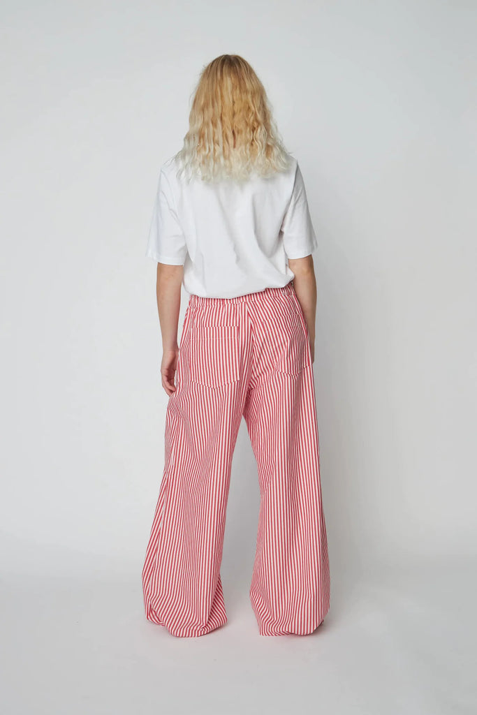 Oversizowe, bawełniane spodnie w czerwono-białe paski Oversized Striped STELLA NOVA z szerokimi i długimi nogawkami ściąganymi u dołu za pomocą gumek. Spodnie mają wysoki stan i elastyczną talię.
