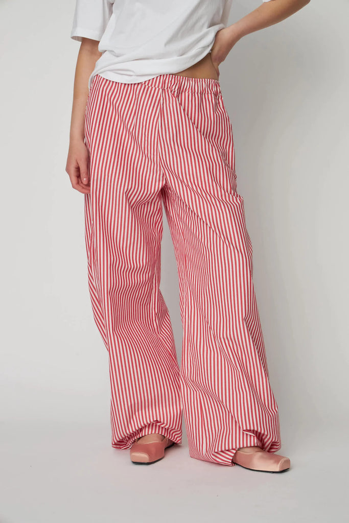 Oversizowe, bawełniane spodnie w czerwono-białe paski Oversized Striped STELLA NOVA z szerokimi i długimi nogawkami ściąganymi u dołu za pomocą gumek. Spodnie mają wysoki stan i elastyczną talię.