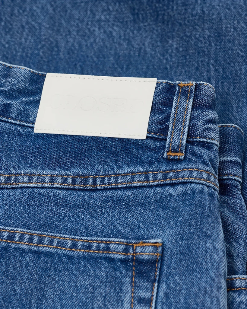 Granatowe jeansy Nikka CLOSED ze średnim stanem i luźną, długą luźną, prostą nogawką. Przylegające w biodrach. Posiadają pięć kieszeni. Przy rozporku mają niewielką, charakterystyczną naszywkę z logo marki