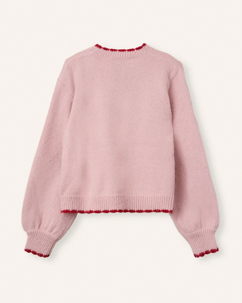 Sweter Freja Rose Strawberry marki Helmstedt w uroczym jasnoróżowym kolorze z motywem truskawki na przodzie. Posiada czerwone ściągacze przy mankietach i dole, które idealnie komponują się z printem na środku. 