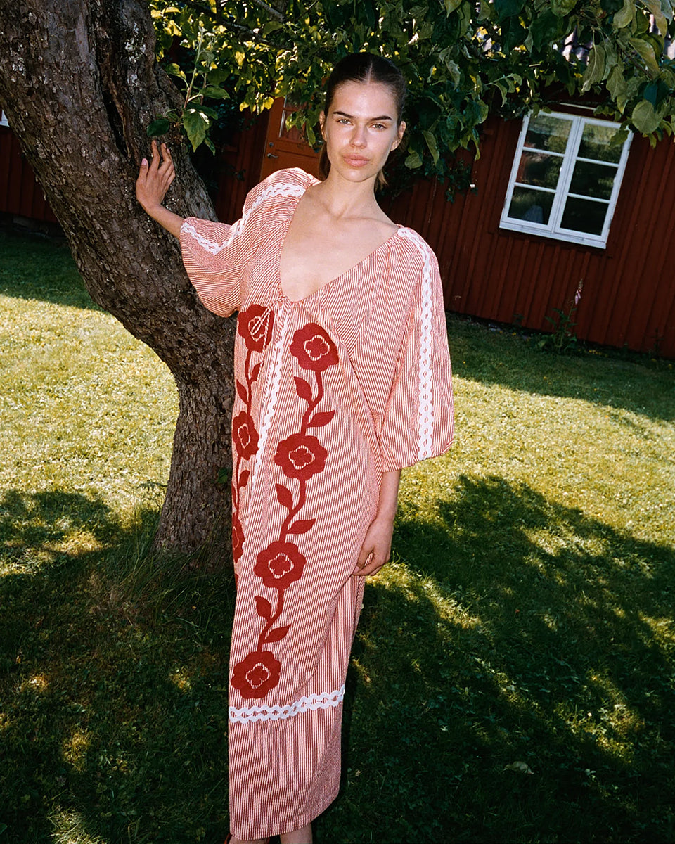 Szeroka, luźna sukienka Abelone Red Flower marki SISSEL EDELBO z obszernymi rękawami typu raglan z elastycznymi otworami i szerokim dekoltem w serek, który ściągany jest regulowanym sznurkiem. Posiada miękką podszewkę, która nadaje bufiasty kształt. Ozdobiona jest wyrazistym, kwiatowym haftem oraz szerokimi, zygzakowatymi taśmami. Wykonana w 100% z jakościowej bawełny organicznej.&nbsp;

-Luźny, szeroki krój

-Kwiatowy haft

-Ściągany dekolt w serek

-ONE SIZE