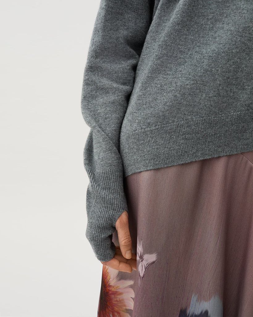 Cienki, szary sweter Acer Light Grey Melang z wycięciem na jednym ramieniu i otworami na kciuki w wydłużonych rękawach. Ma asymetryczny dół, który pozwala na różnorodne stylizacje z dopasowanymi spodniami lub spódnicą. Wykonany z miękkiej dzianiny z wełny merino.&nbsp;