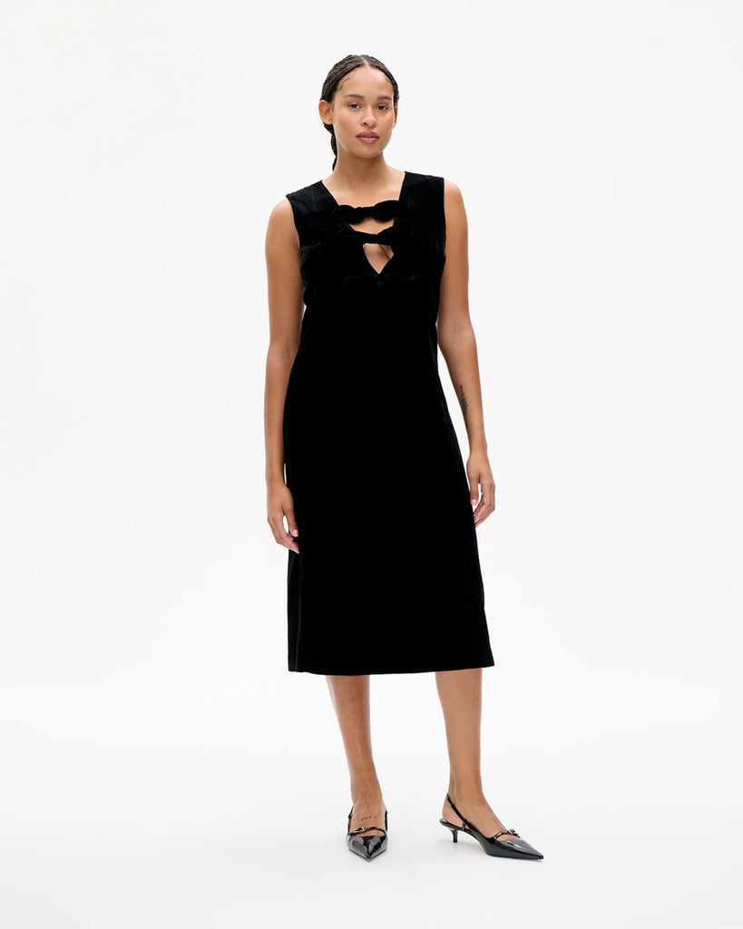 Aksamitna, dopasowana sukienka Ajka Black Velvet bez rękawów. Zdobiona dekoltem w serek z kokardkami. Zapinana na zamek z tyłu. Wykonana z miękkiej mieszanki wiskozy. Długość midi. Idealna romantyczna i zarazem nowoczesna propozycja na wyjątkowe okazje.&nbsp;